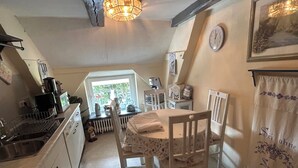 A cozy kitchen with white cabinets, a wooden table, and a radiator. There is a window with a view of greenery outside.