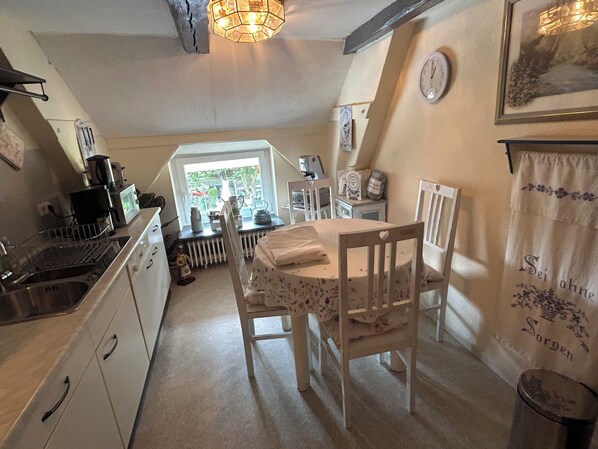 A cozy kitchen with white cabinets, a wooden table, and a radiator. There is a window with a view of greenery outside.