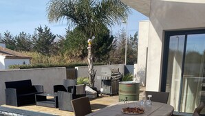 A wooden deck with a dining table and chairs, a barbecue grill, and a swimming pool.