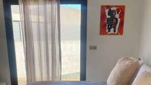 A bedroom with a bed, a window with curtains, and a wall-mounted artwork.