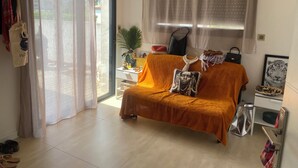 A living room with a sofa, a coffee table, a plant, and a window with curtains.
