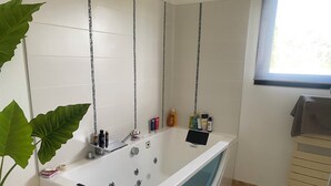 A modern bathroom with a bathtub, a sink, and a mirror. There are toiletries on the sink and a plant next to the bathtub.