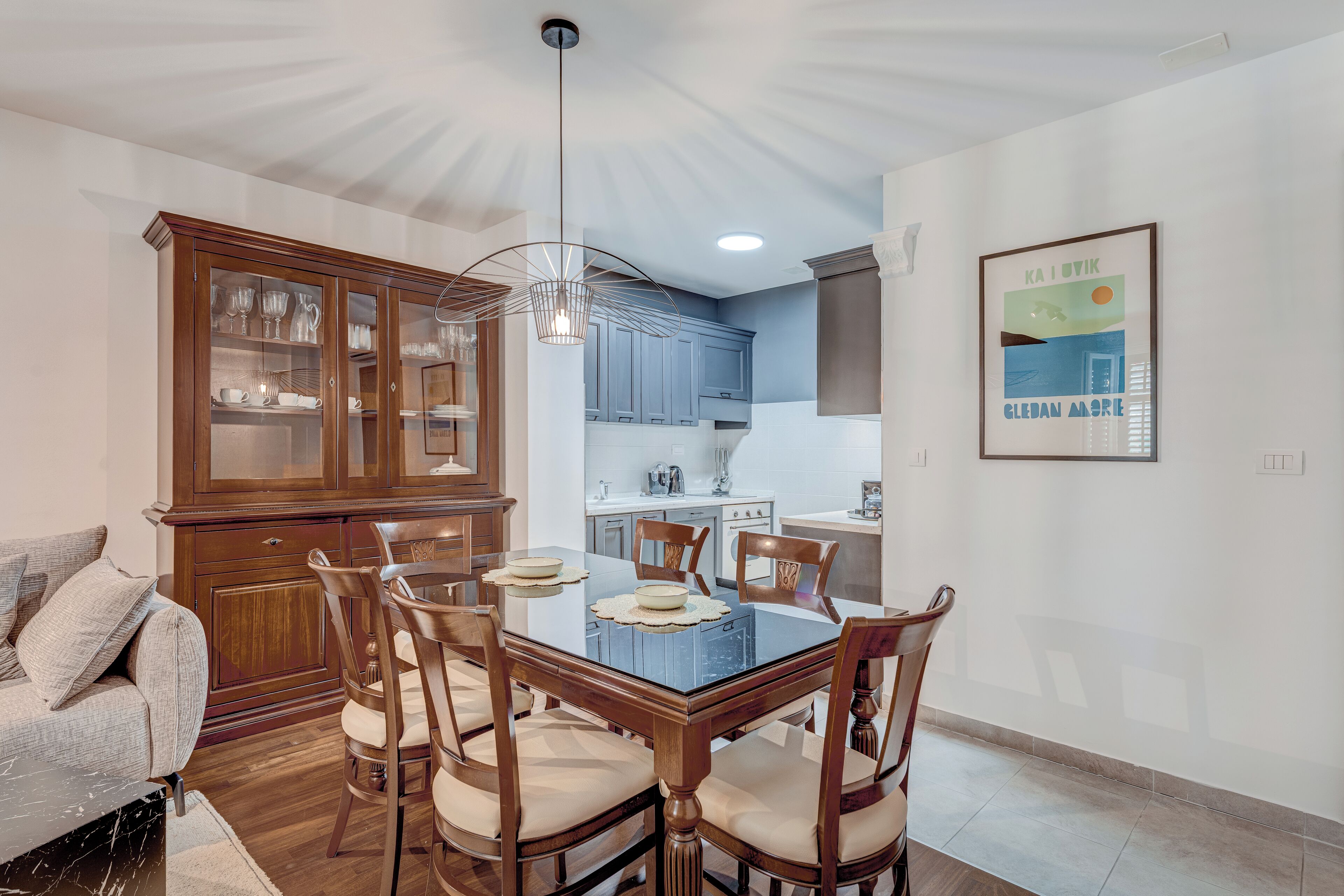 A dining area with a glass-top table, wooden chairs, and a cabinet with glass doors.