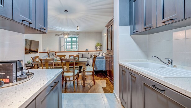 Une cuisine moderne avec des meubles gris, un plan de travail blanc et un coin repas comprenant des chaises en bois et un canapé.