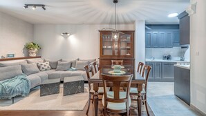 Un salon moderne comprenant un canapé, une table à manger et des chaises, un meuble en bois, ainsi qu’un coin cuisine avec des placards et des appareils électroménagers.