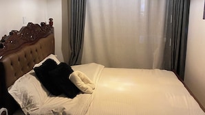 Une chambre d’hôtel avec un lit, des rideaux, un luminaire suspendu et un radiateur fixé au mur.
