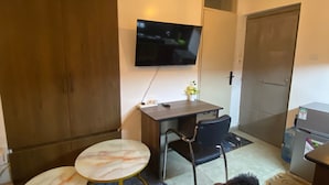 Un espace de vie compact comprenant un canapé, une petite table à manger, un téléviseur fixé au mur et une armoire.