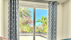 Un balcón con dos sillas, una mesita, un vaso de bebida y vistas a plantas tropicales y una palmera.