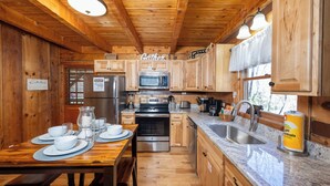 A wooden cabin-style kitchen with a dining table set for four, equipped with a refrigerator, microwave, and stove.