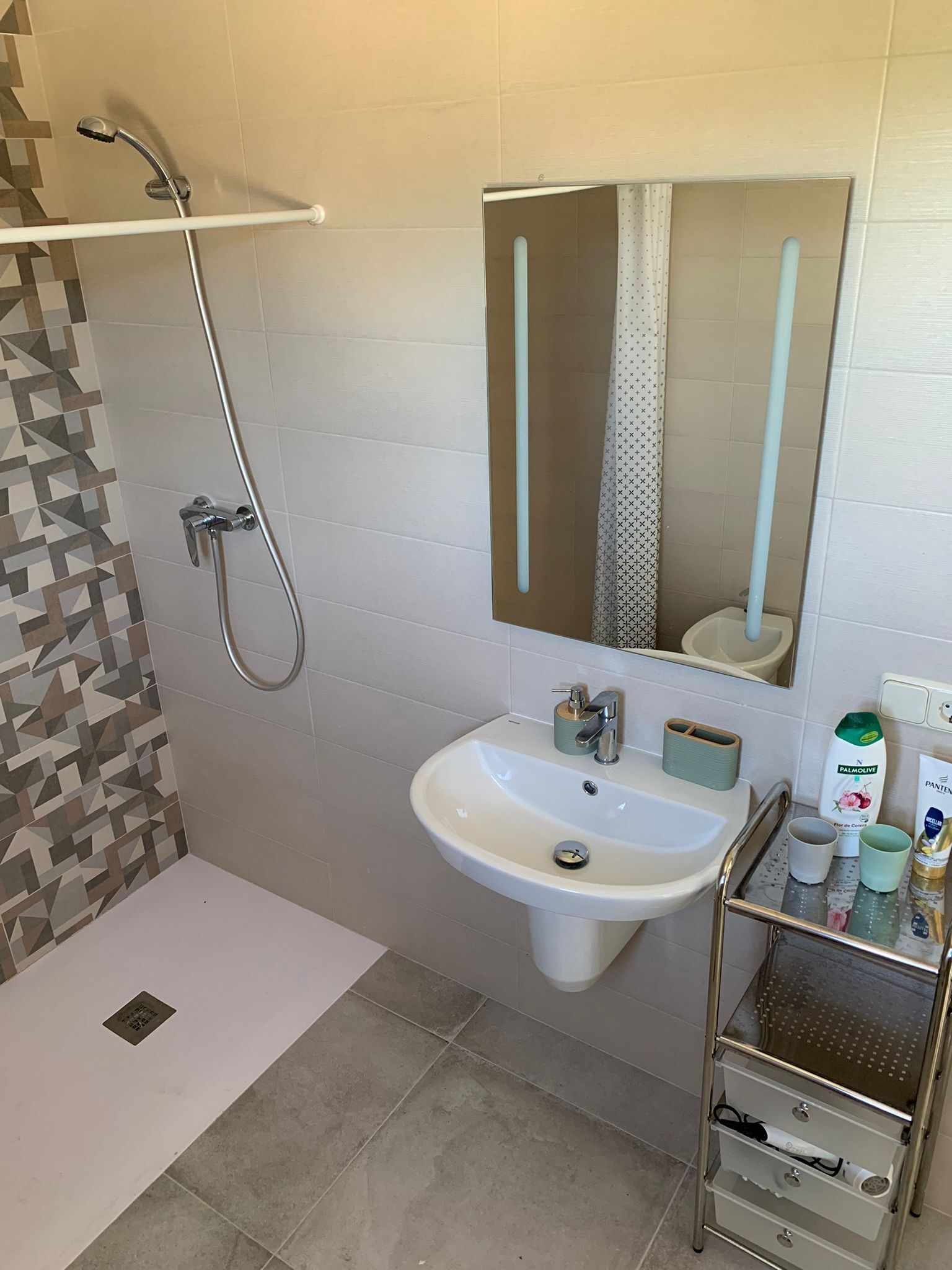 Un bagno con doccia, lavandino, specchio e ripiano con articoli da toilette.