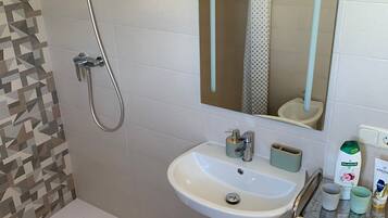 A bathroom with a shower, a sink, a mirror, and a shelf with toiletries.