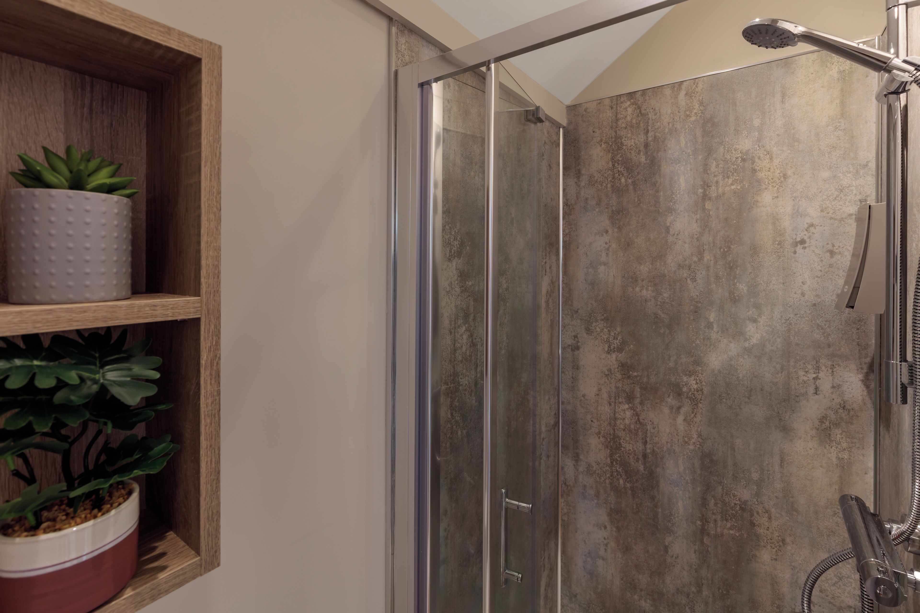Un box de ducha con puerta de vidrio, un estante de madera con plantas en macetas y un cabezal de ducha.