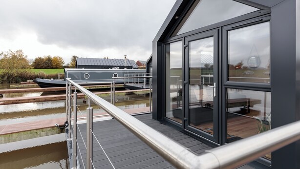 A modern building with large windows overlooking a canal, a boat docked nearby, and a wooden deck. - Tattenhall Marina (Chester)