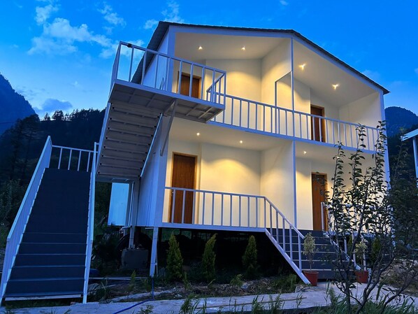 A two-story building with a balcony on the upper floor, a staircase leading to the upper level, and a door on the ground floor. - Harsil Village Resort (Bhatwari)