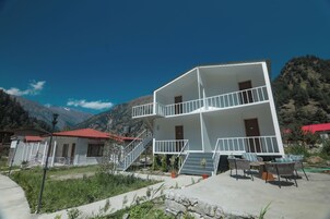 Un edificio de dos pisos con balcón, mobiliario exterior y montañas al fondo.