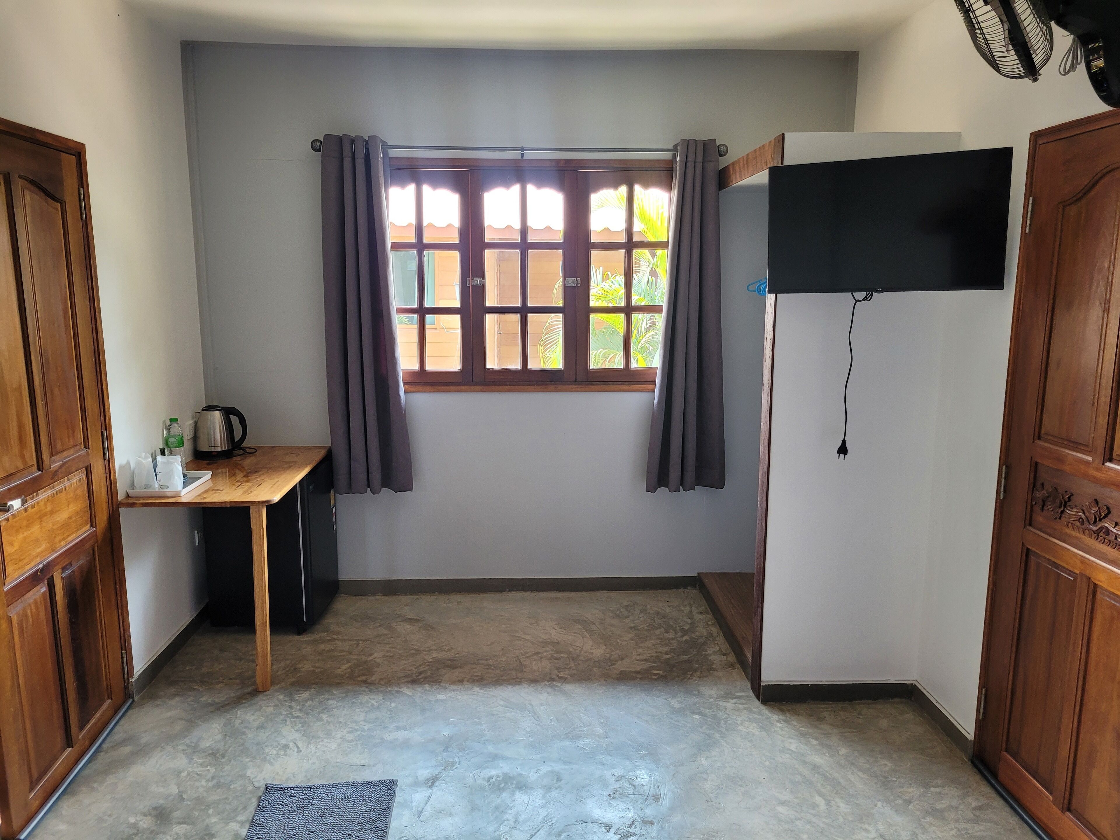 A small room with a window, a desk, a television, and a wardrobe.