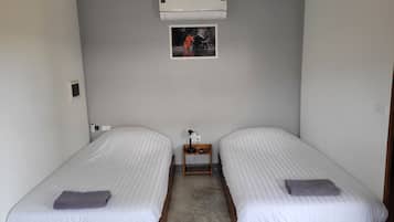 A room with two single beds, a small bedside table with a lamp, an air conditioner, and a framed picture on the wall.