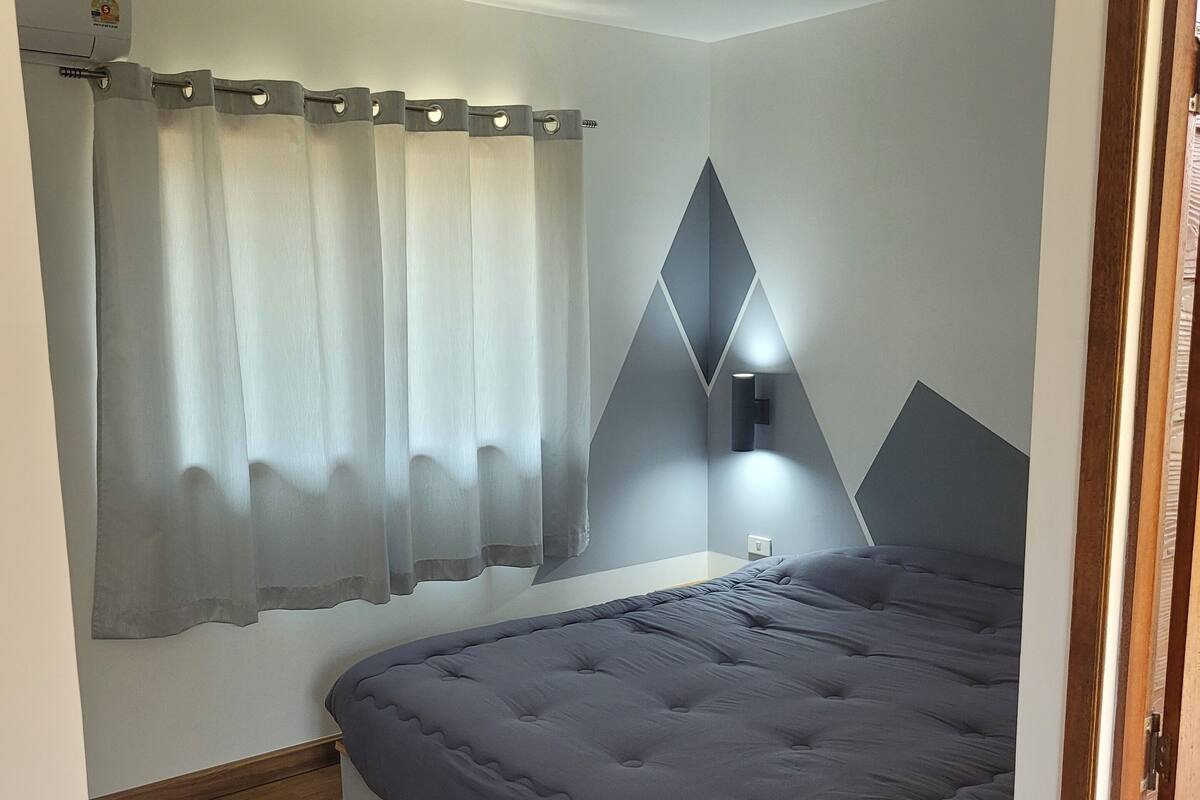 Une chambre à coucher avec un lit, des rideaux, une lampe fixée au mur et un plancher en bois.