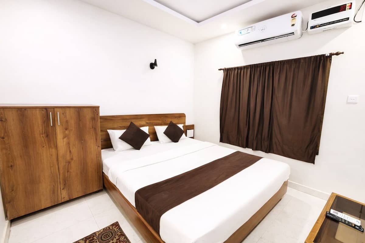 Une chambre d’hôtel avec une armoire en bois, un lit avec une literie blanche et marron, un appareil de climatisation et une fenêtre avec des rideaux marron.