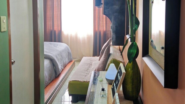 A hotel room with a bed, a bedside table with a vase of flowers, a mirror, and a ceiling light fixture.