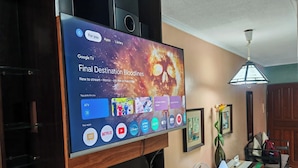 A television mounted on a wall displaying a streaming service interface with various app icons and a movie title.
