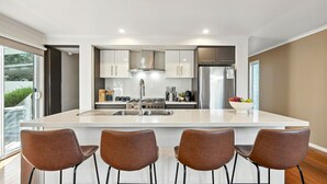 Una cocina moderna con una isla central, electrodomésticos de acero inoxidable y cuatro sillas marrones.