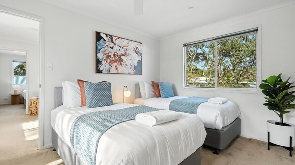 Habitación de hotel moderna con dos camas, un ventanal con vistas a árboles y un cuadro en la pared.