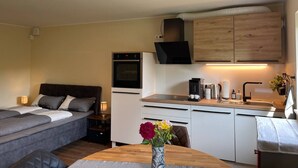 Un espacio habitable compacto con kitchenette, cama, mesa de comedor con flores y televisor sobre los gabinetes.