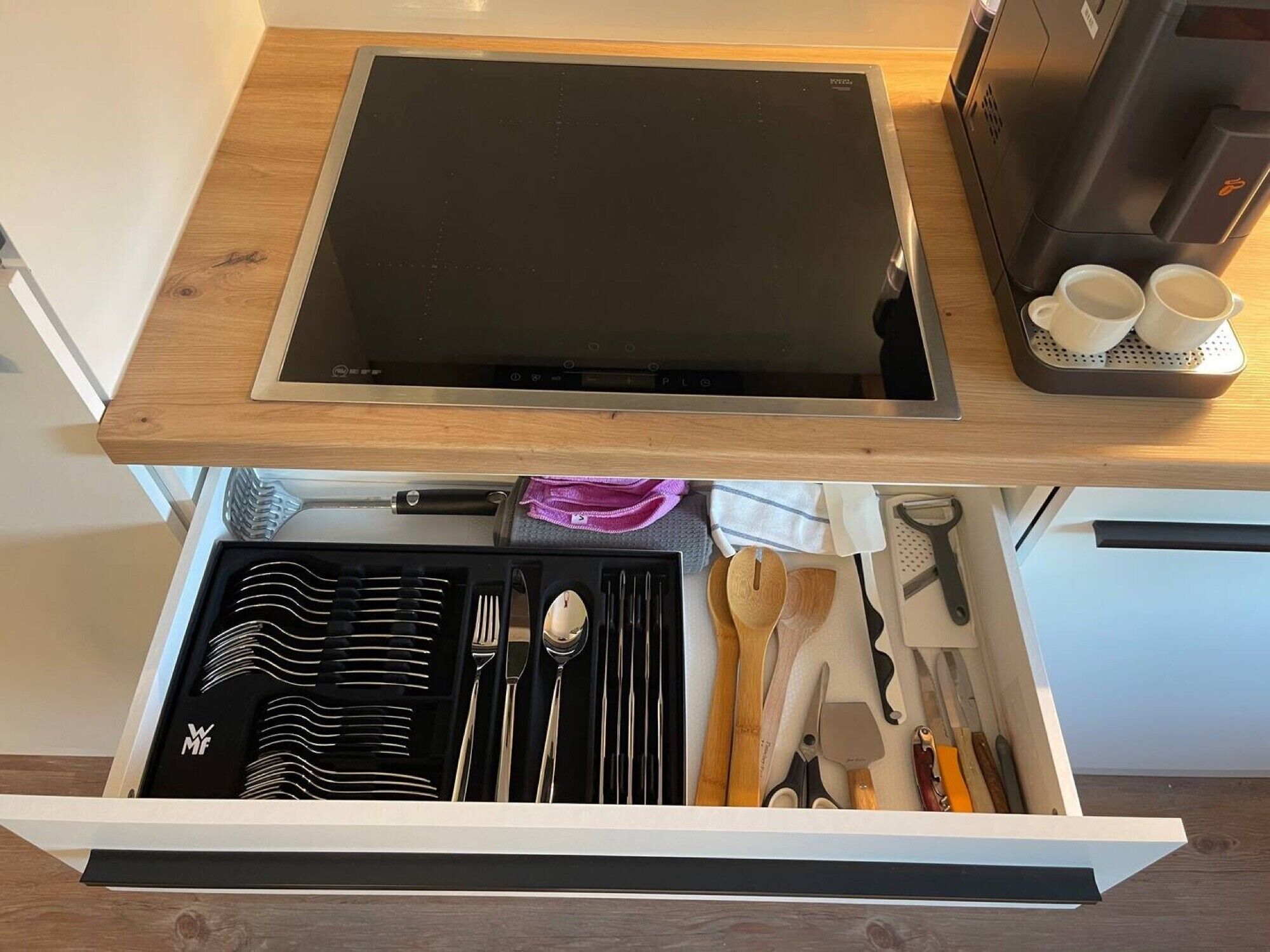 A kitchen drawer with utensils, a coffee maker, and a tray with cups.
