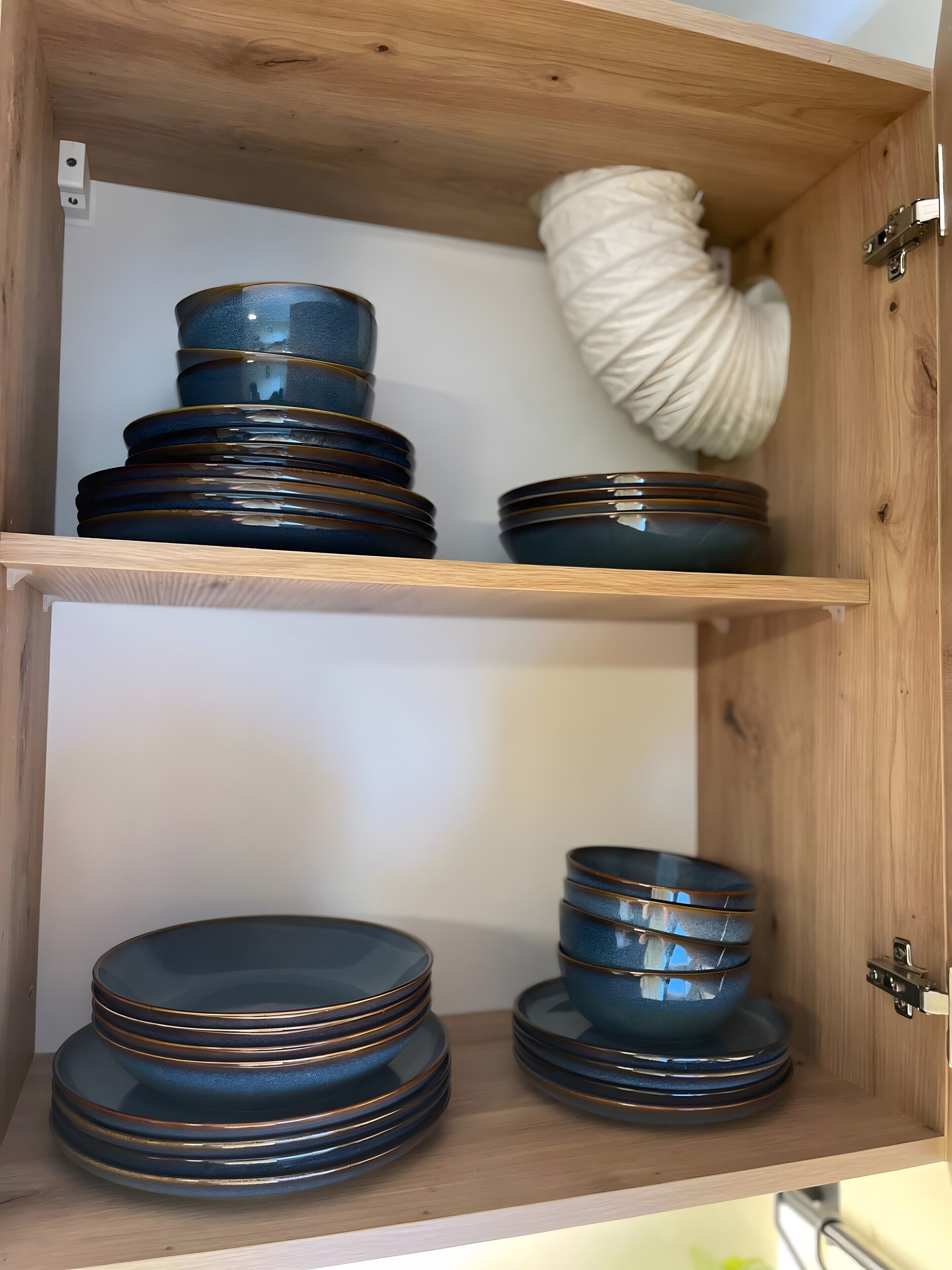 Un meuble en bois doté d’étagères où sont empilées des assiettes, ainsi qu’un objet décoratif blanc.