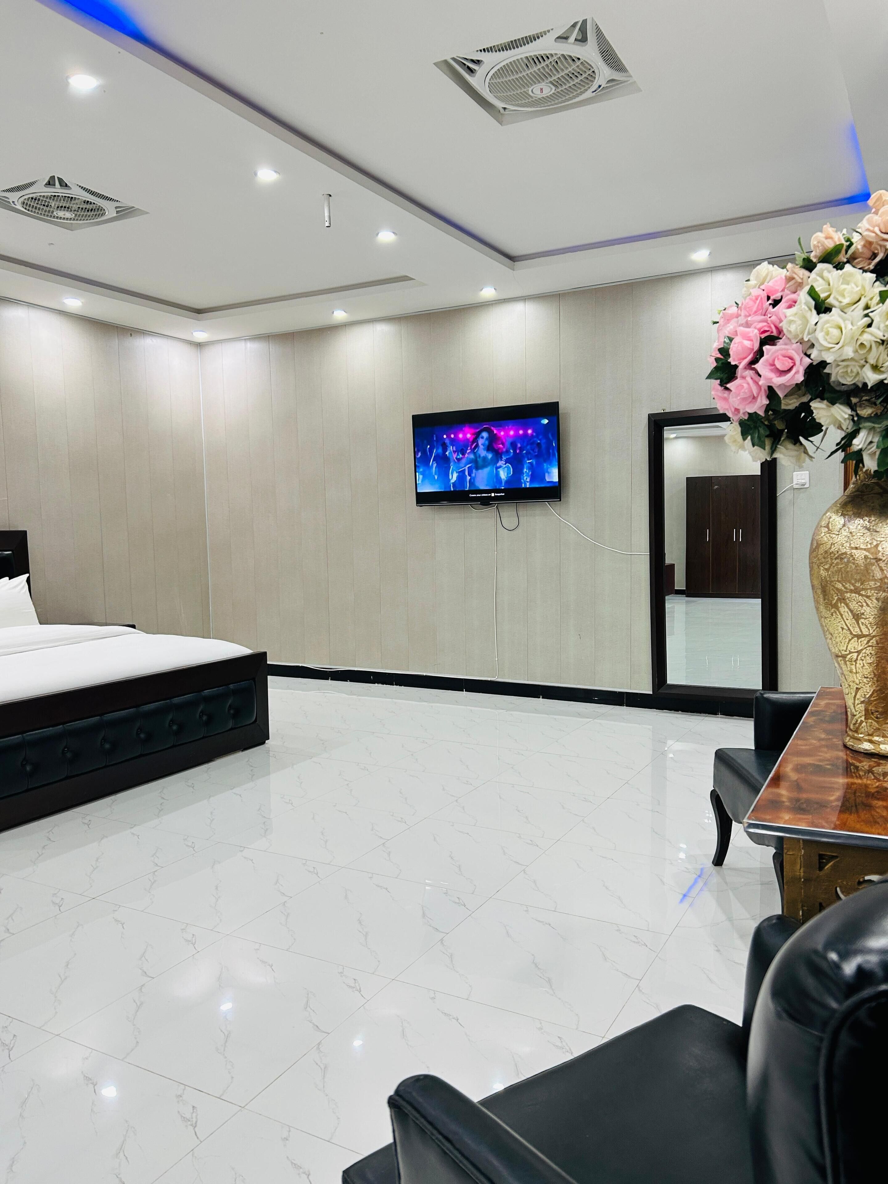 Une chambre d’hôtel moderne, équipée d’un lit, d’un téléviseur fixé au mur, d’un grand vase rempli de fleurs et d’un miroir.