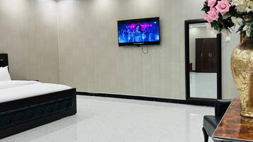 Une chambre d’hôtel moderne, équipée d’un lit, d’un téléviseur fixé au mur, d’un grand vase rempli de fleurs et d’un miroir.