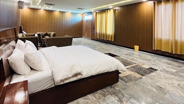 Habitación de hotel con una cama grande, un área de estar con sillas, una pared de madera y un piso con diseño.
