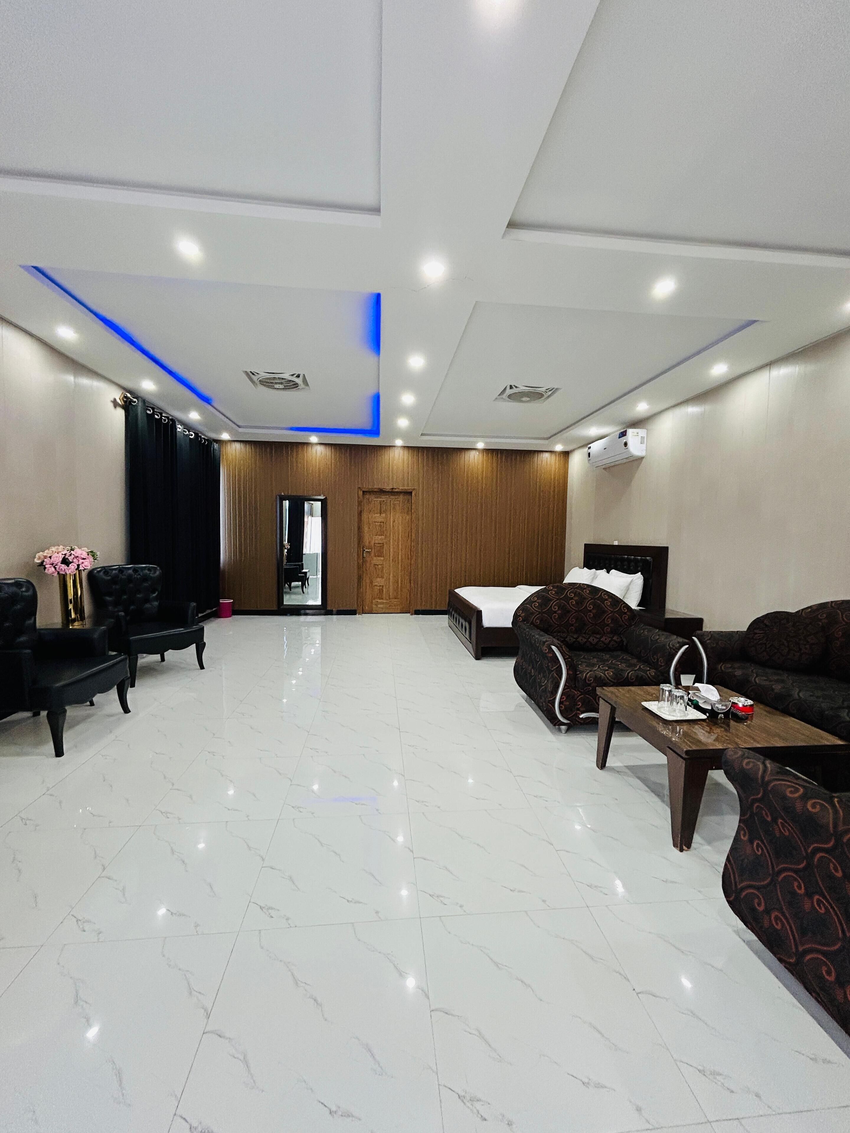 A modern hotel room with a marble floor, a sofa set, a dining table, and a wooden accent wall.