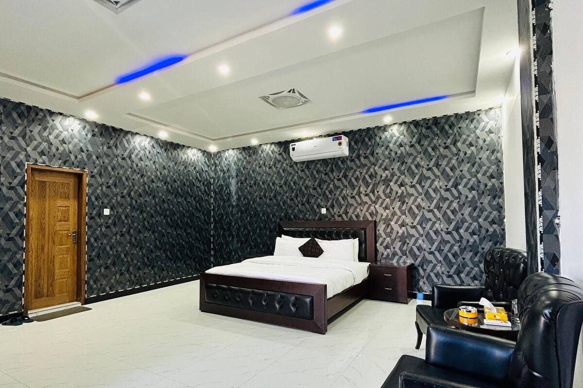 A modern bedroom with a large bed, a black leather armchair, a small table, and a ceiling fan.
