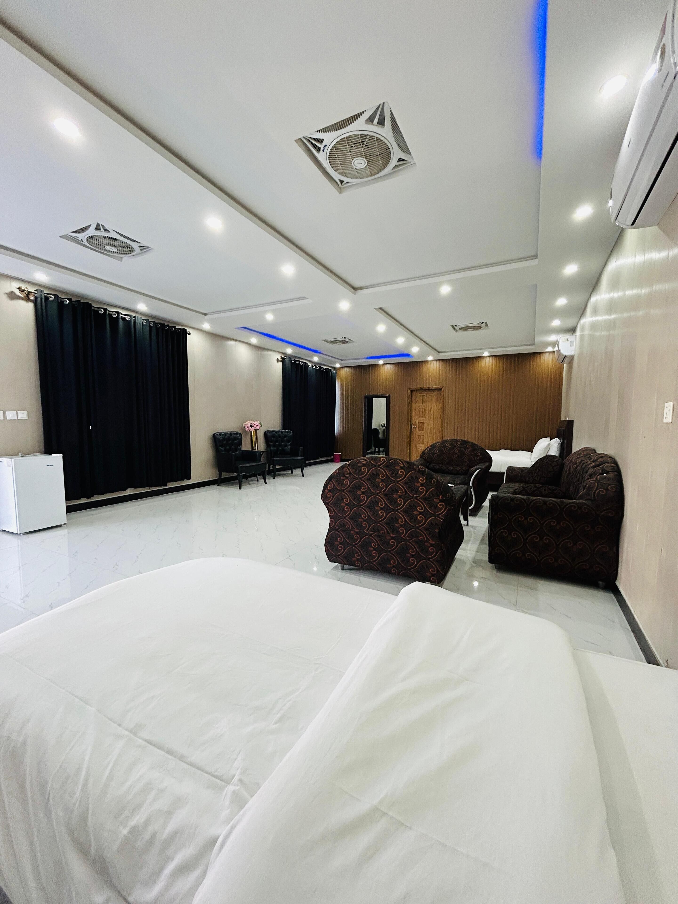 A hotel room with a large bed, two patterned armchairs, a small table, and a mirror.