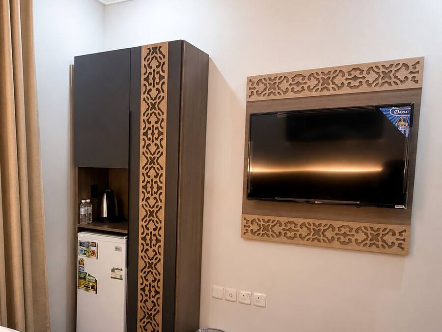 A hotel room with a bed, a minibar, a television, and a trash bin.