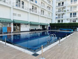 A swimming pool with a tiled deck, surrounded by a white railing and a chain barrier.