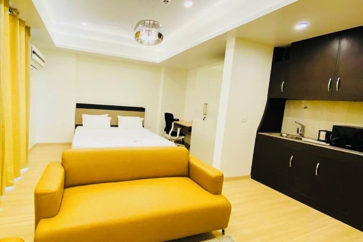 Una habitación de hotel con una cama, un sillón amarillo, un escritorio y una kitchenette.