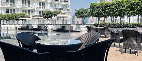 A rooftop terrace with outdoor seating, a glass table, and a view of a white building with multiple balconies.