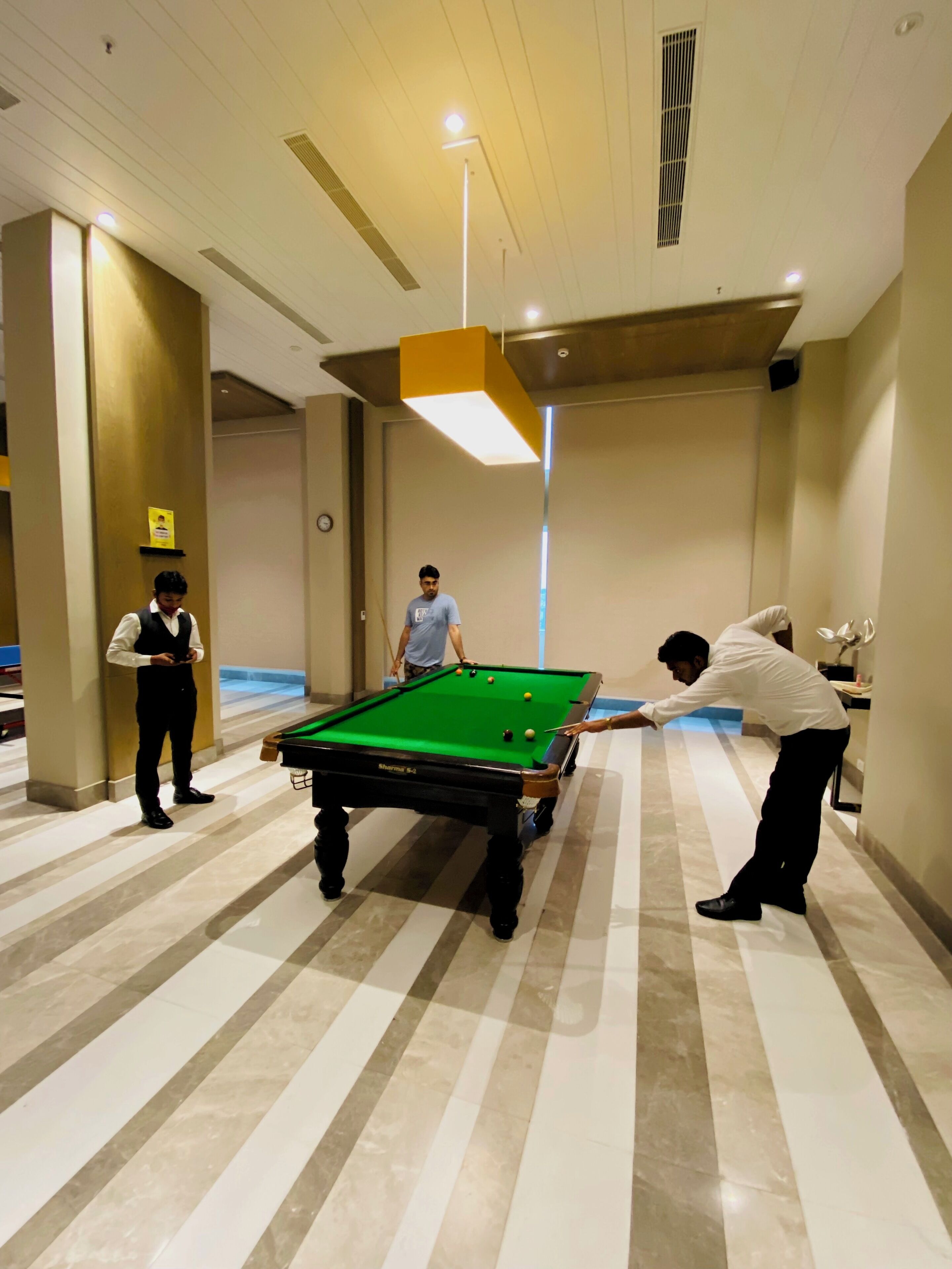 A pool table in a hotel lobby with a striped floor pattern.