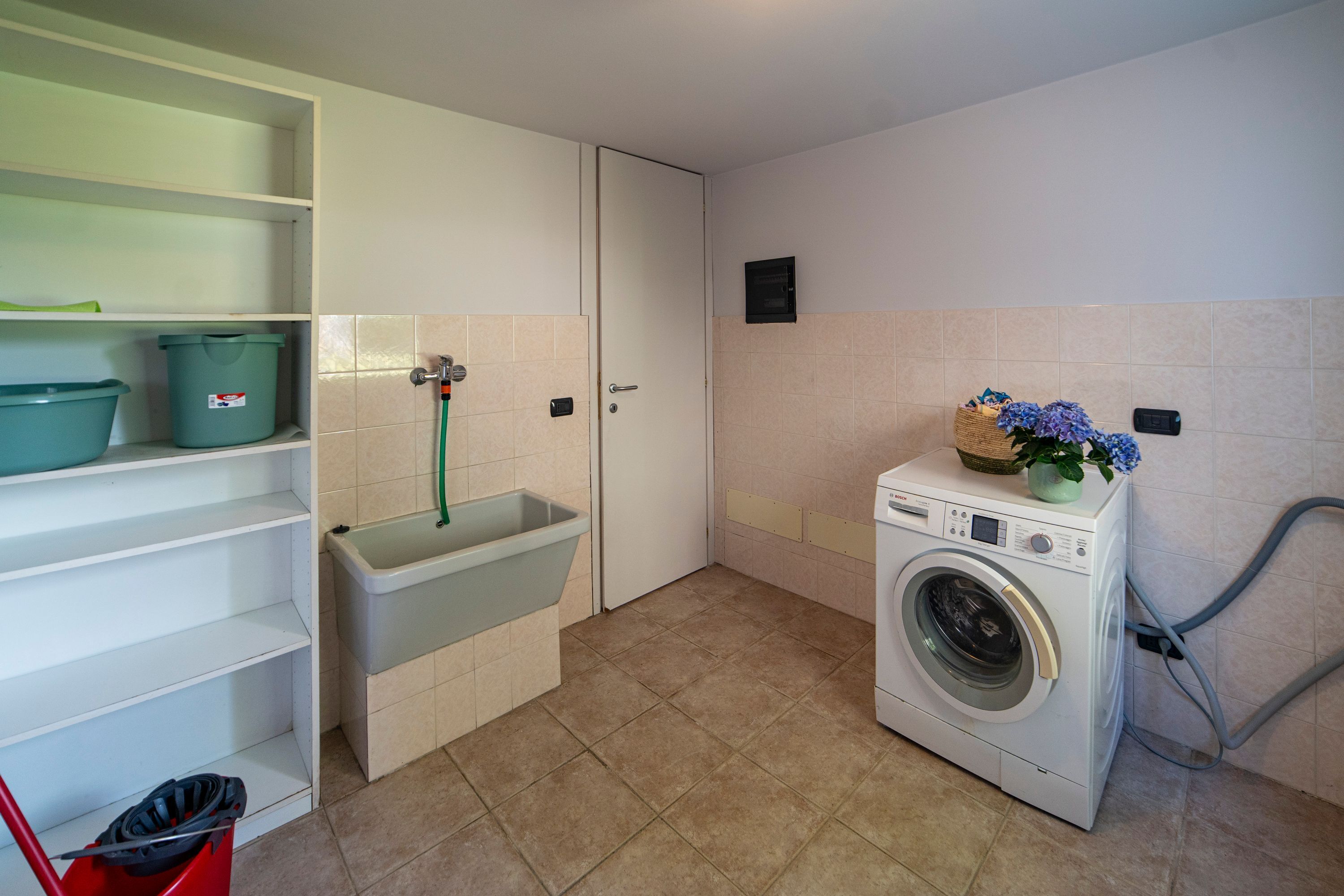 A laundry room with a washing machine, a sink, and shelves with storage bins.