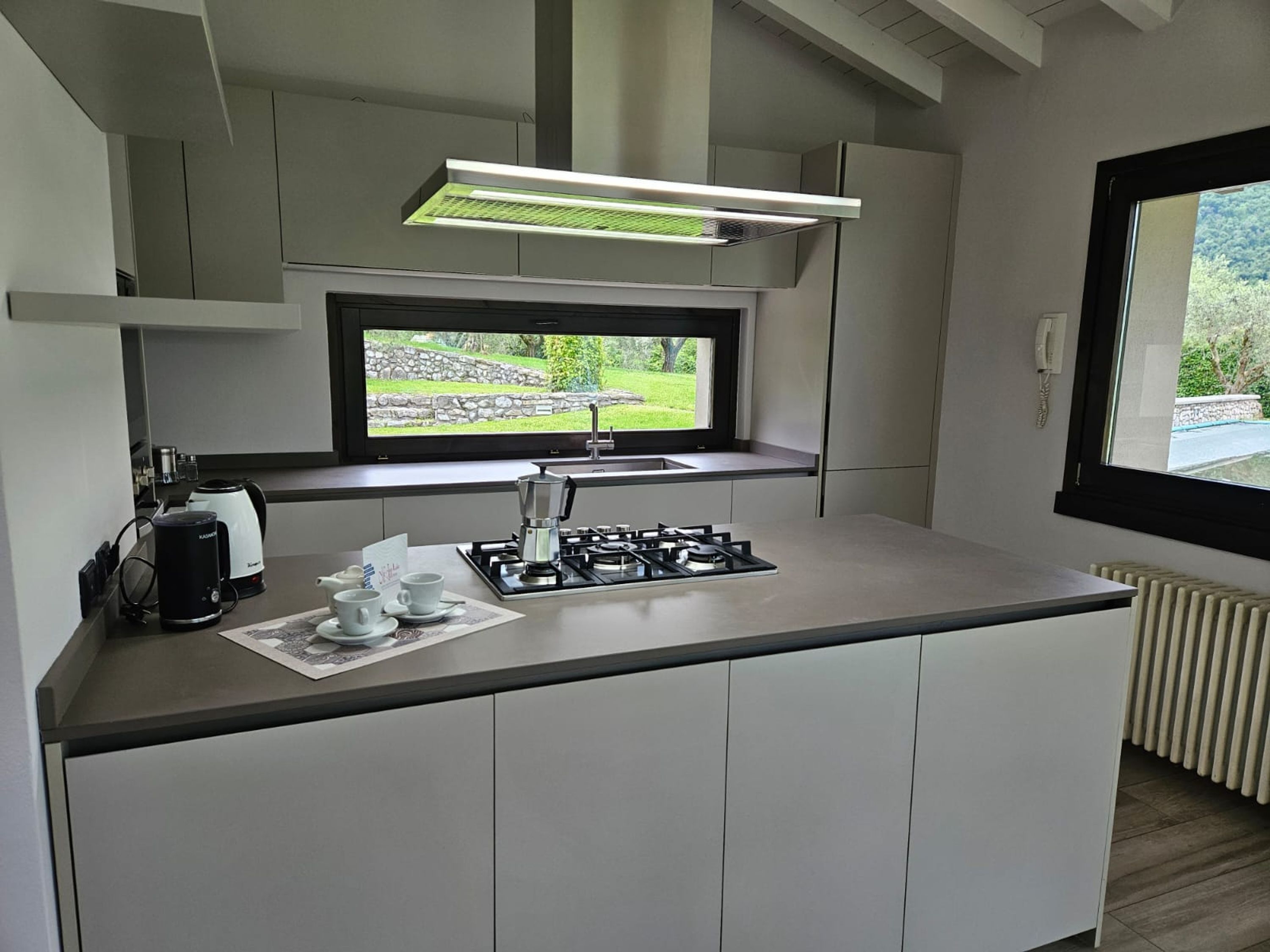 A modern kitchen with a gas stove, coffee maker, and a window with a view of greenery.