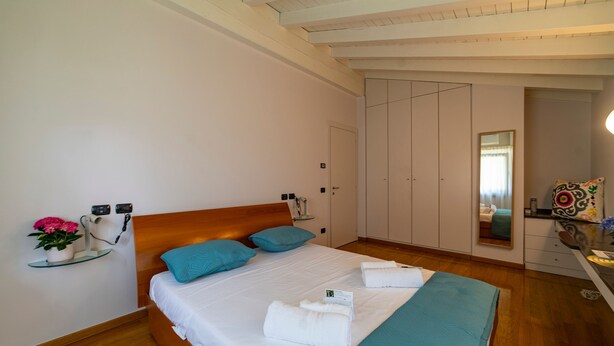A neatly made bed with white linens and blue pillows, a bedside table with a flower vase, and a wooden headboard. - Villa Anna Lake View (Iseo)