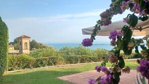Een tuin met uitzicht op zee, een klein torentje en een pergola met paarse bloemen.