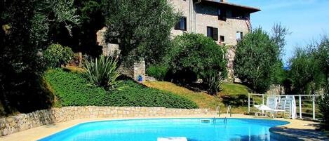 A swimming pool with a stone wall and a white lounge chair.