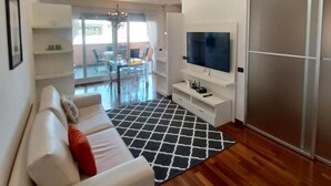 Een moderne woonkamer met een witte bank, een zwart-wit tapijt, een flatscreen televisie en een schuifdeurkast.