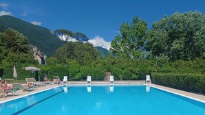 Een rechthoekig zwembad met helderblauw water, omgeven door een betegeld zonnedek. Er staan ligbedden en parasols langs de zwembadrand.