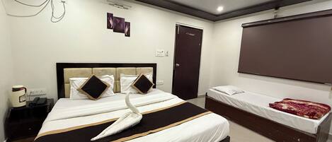 A hotel room with a large bed, a smaller bed, a desk, a chair, a telephone, and a wall-mounted TV.