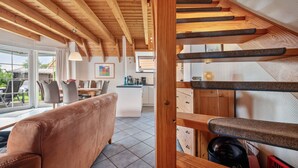 Un intérieur moderne avec un escalier en bois, un canapé, un coin cuisine et un espace repas doté de grandes fenêtres.